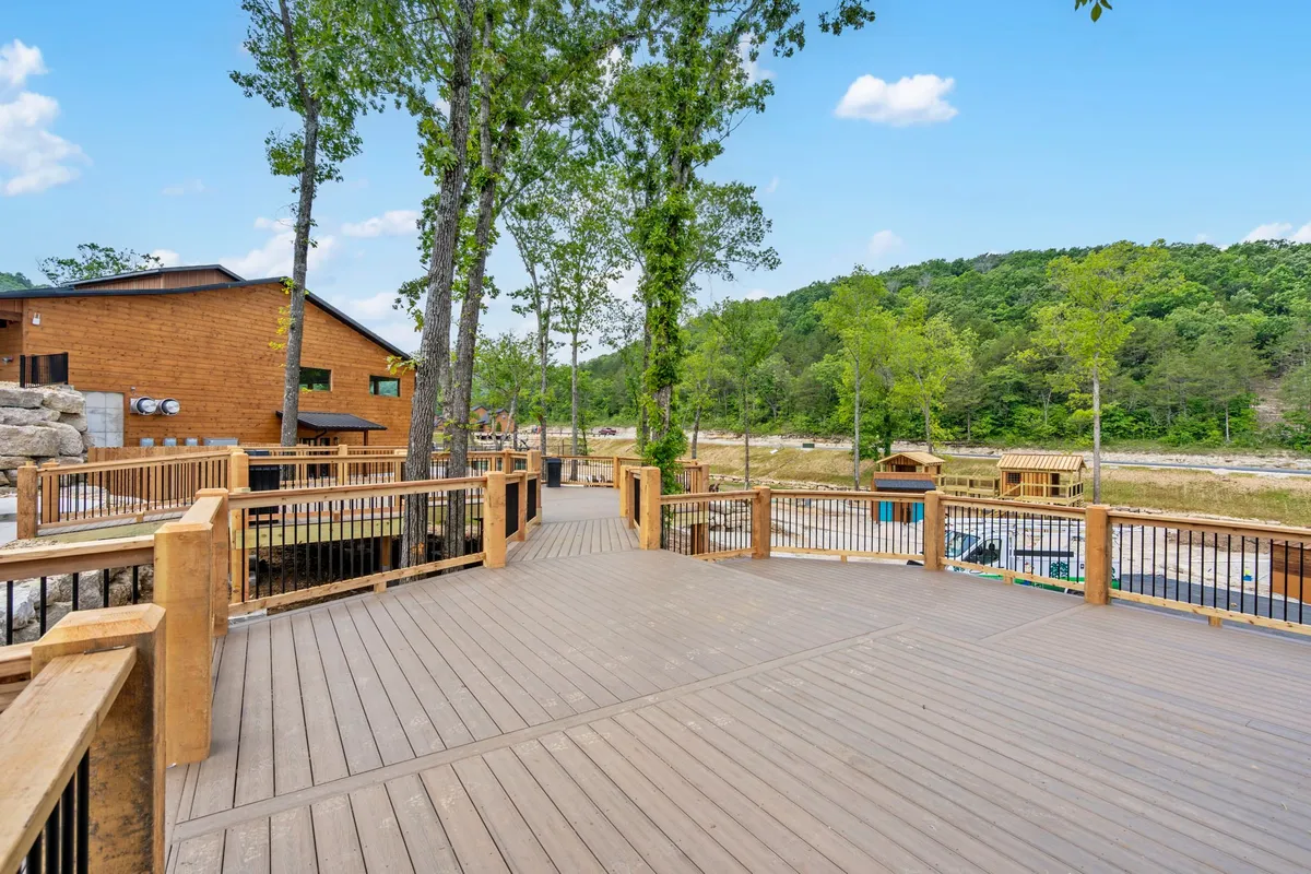 A peaceful wooden deck surrounded by tall trees, with outdoor seating ideally positioned to enjoy the forest view. The deck offers an inviting atmosphere for either solo relaxation or gathering with friends, bathed in natural light and immersed in the serene Ozark landscape.