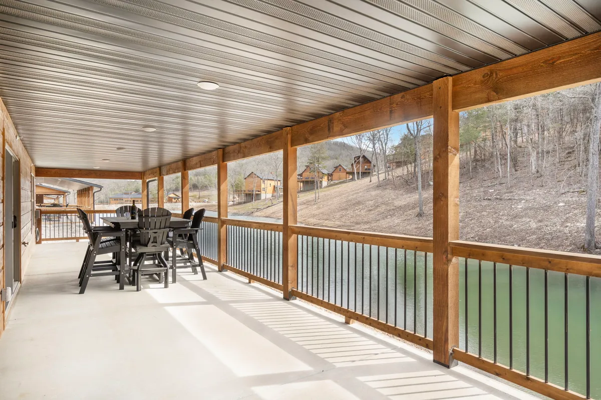 A wooden deck with an outdoor dining table overlooks a tranquil lake, bordered by a wooden railing. The peaceful setting is perfect for relaxing, dining, or watching wildlife with sweeping views of the water and countryside.