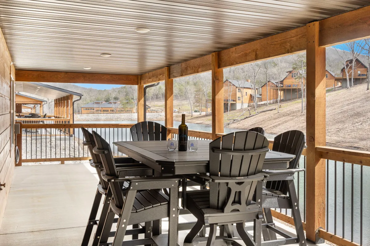 An outdoor dining table set for a meal, complete with a bottle of wine and surrounded by a wooden railing. The space overlooks a beautiful natural landscape, ideal for sharing moments with loved ones or enjoying quiet reflection.